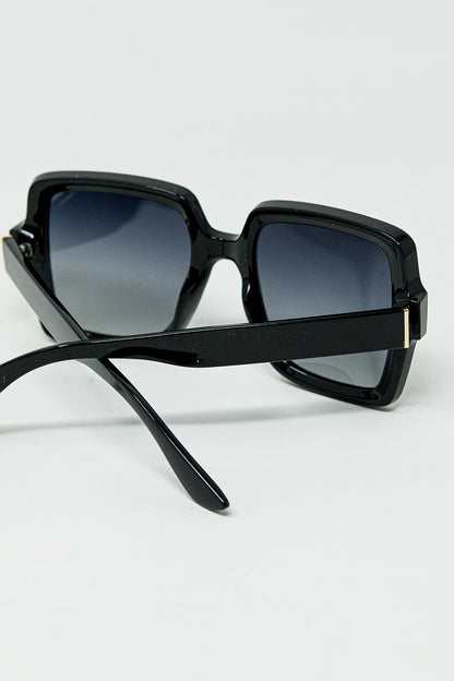 Gafas de sol de montura cuadrada ancha con detalle dorado en las patillas.