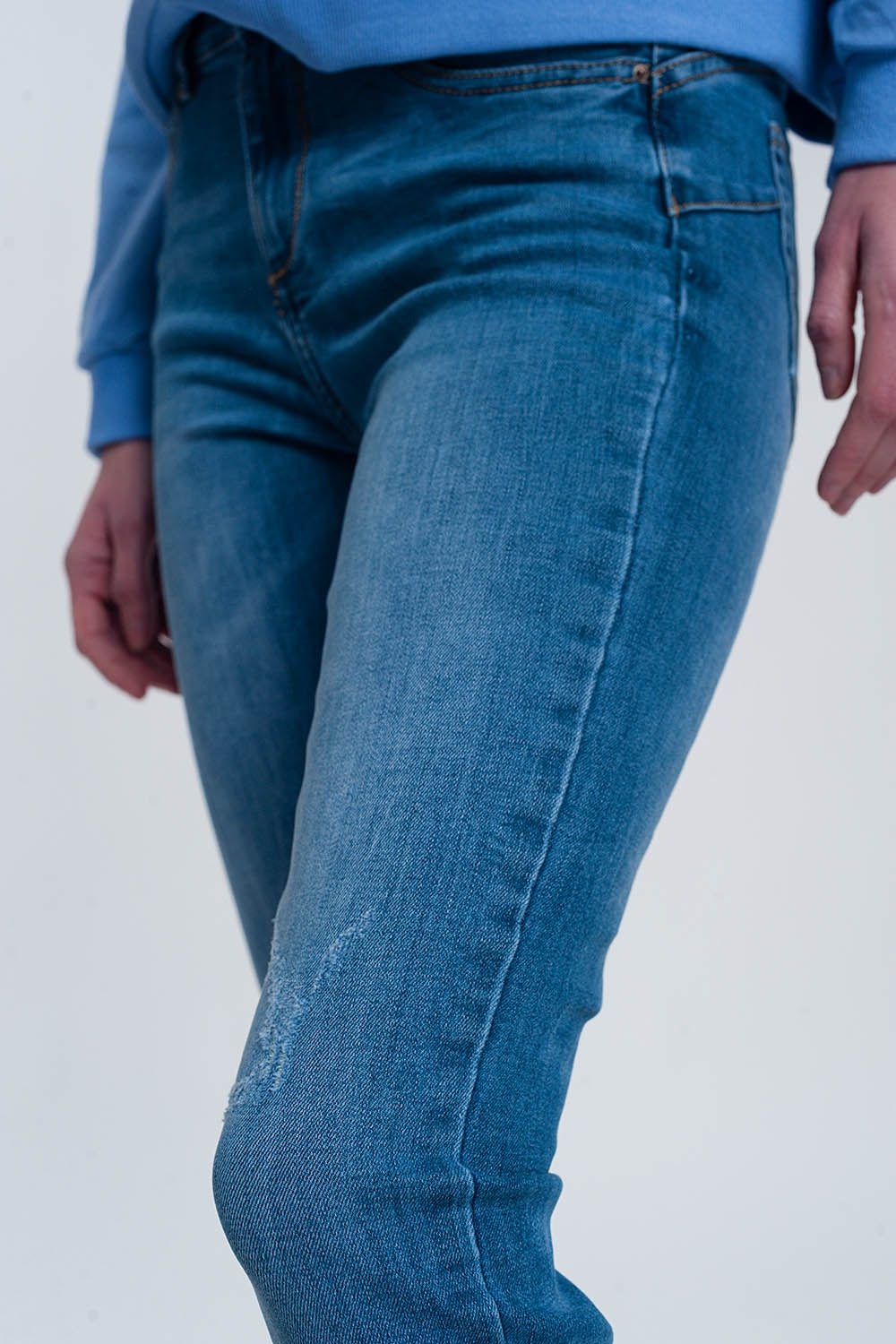 jeans ajustados de mezclilla clara con tobillos doblados y detalle rasgado